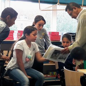 Students look at family archives held by an adult in a classroom