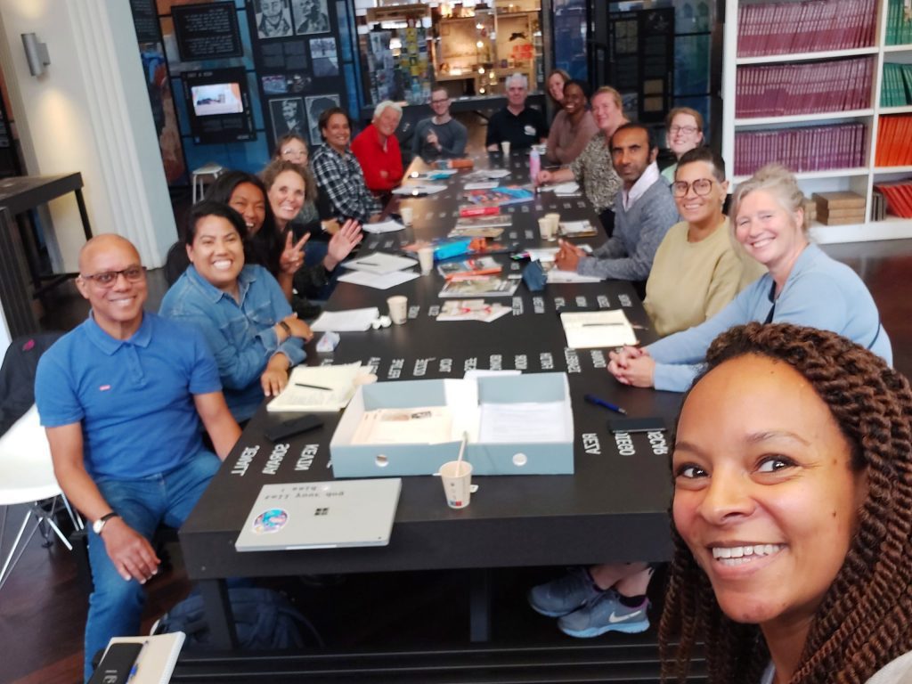 A group of smiling adults sit around a table and pose for a selfie