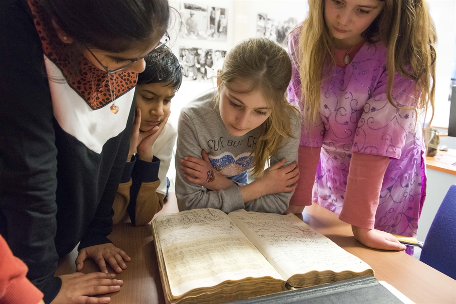 Teach history with archives: 4 students gather around a book at the archives