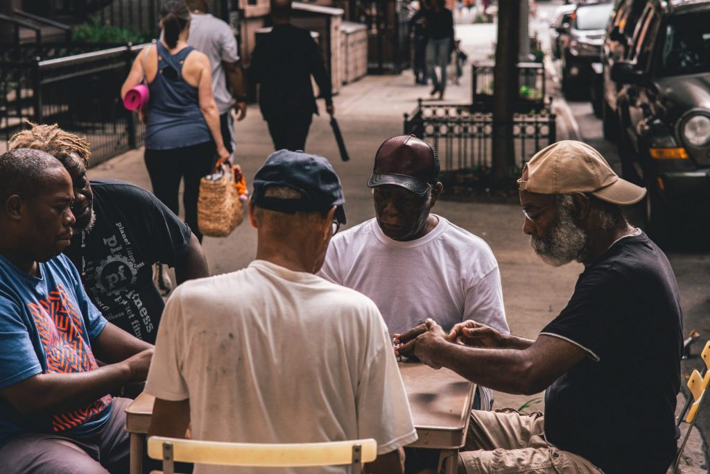 5 men sitting outside play a game at a table