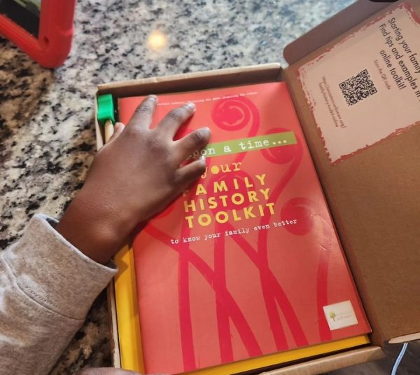 A young hand reaches into the Family History Toolkit, with the colourful booklet on top