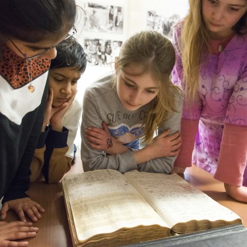 Four children look at a large book in an archive