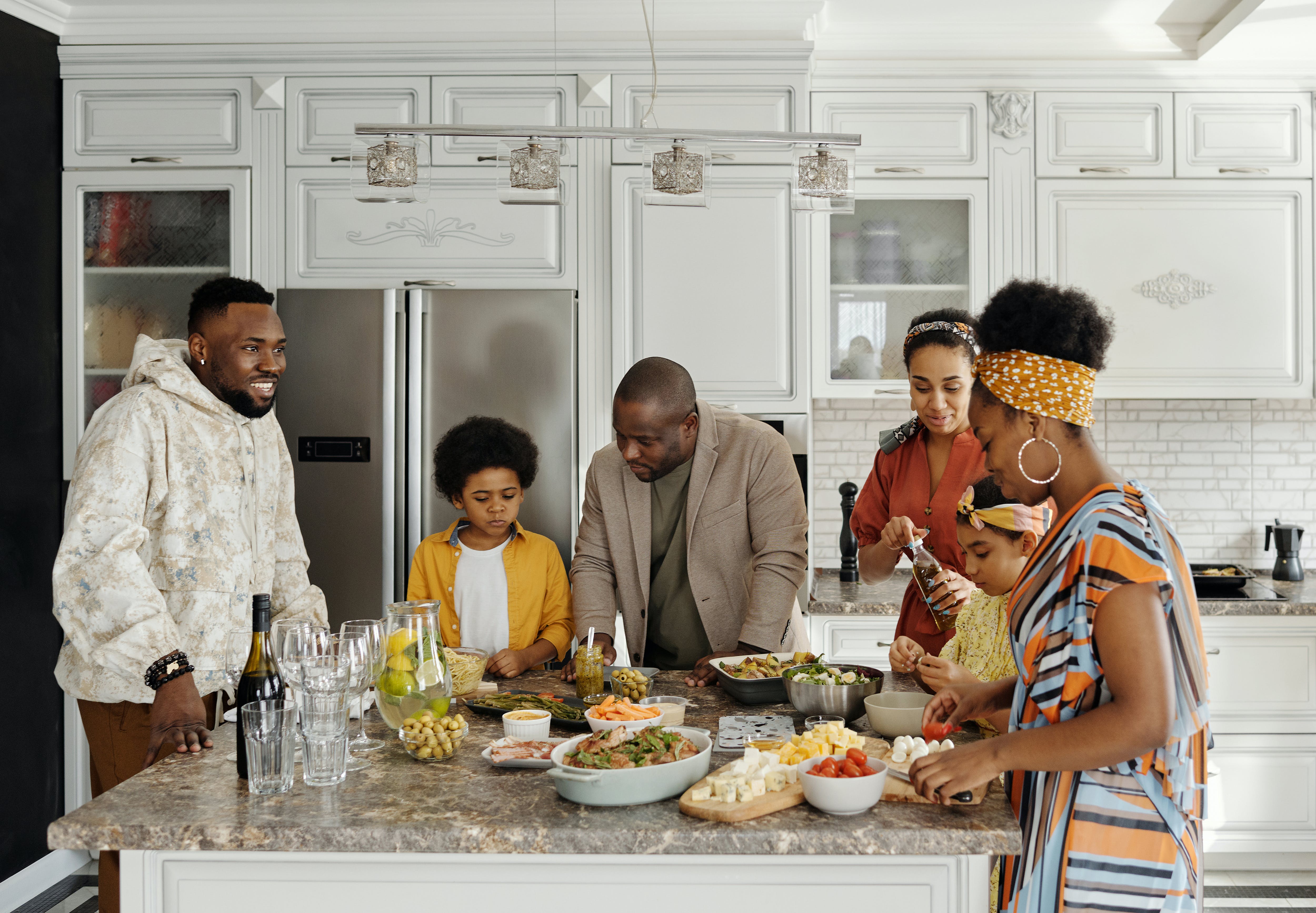 A family of six gather and talk around food in a kitchen