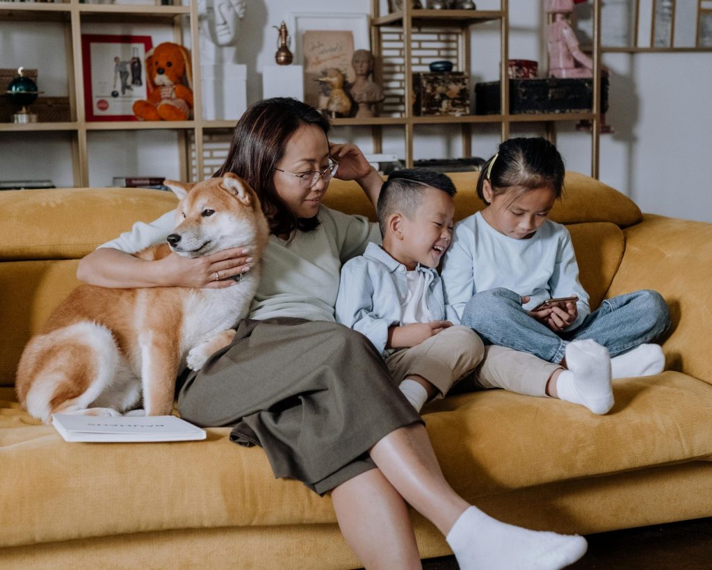 A mother and two children look at a phone, while sitting on the sofa with their dog