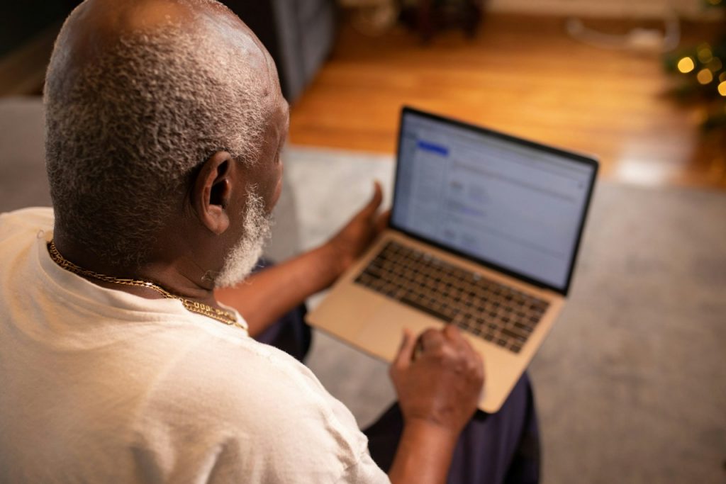 An older man holds an open laptop on his lap